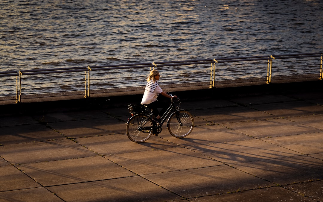 A woman riding a bike down a sidewalk next to a body of water